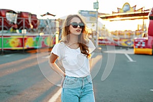 Stylish redhead modern hipster young woman in trendy sunglasses in a white t-shirt in vintage jeans posing