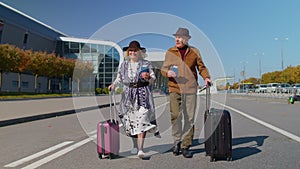 Stylish retired family couple granny grandfather walking with luggage suitcase bags to airport hall