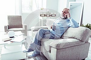 Stylish retired man holding his phone while calling wife from home