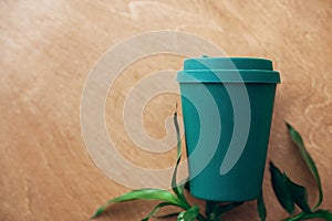 Stylish reusable eco coffee cup and bamboo leaves on wooden background, flat lay. Cup from natural bamboo fiber, zero waste