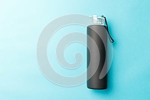 Stylish reusable eco-friendly glass bottle with a black rubberized surface on a blue background. Space for text