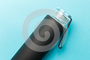 Stylish reusable eco-friendly glass bottle with a black rubberized surface on a blue background. Space for text