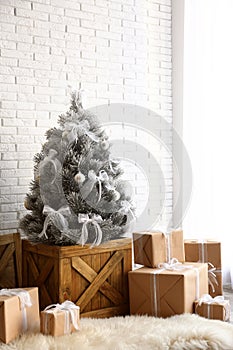 Stylish room interior with beautiful Christmas tree and gifts near brick wall