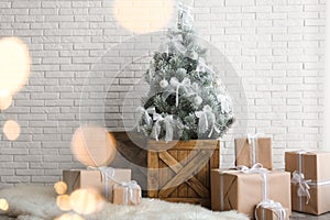 Stylish room interior with beautiful Christmas tree and gifts near brick wall. Bokeh effect