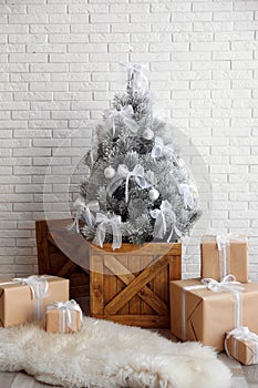 Stylish room interior with beautiful Christmas tree and gifts near white wall