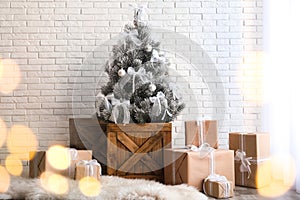 Stylish room interior with beautiful Christmas tree and gifts near white wall. Bokeh effect