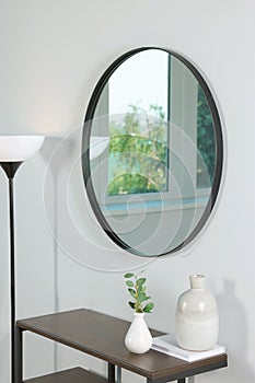 Stylish round mirror on white wall over table in room