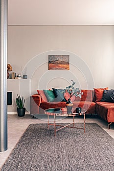 Stylish round table with flowers next to corner sofa with emerald pillows