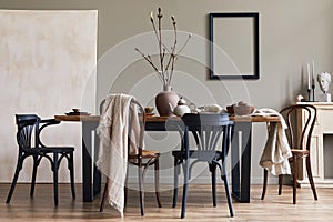 Stylish rustic interior of dining room with walnut wooden table, retro chairs, decoration, fireplace, dried flower, candlestick.