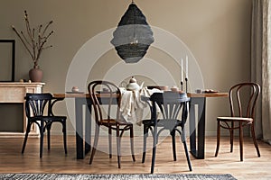 Stylish rustic interior of dining room with walnut wooden table, retro chairs, pedant lamp, fireplace, dried flower, candlestick.