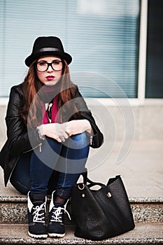 The stylish sad urban girl in sunglasses sits on steps