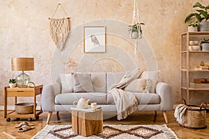 Stylish scandi compostion at living room interior with design gray sofa, wooden coffee table, shelf, cube, carpet, rattan decor. photo