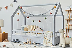 Stylish scandinavian child`s room with creative wooden bed, pillows, wooden cube, lamp, wooden shelf, plush and wooden toys.