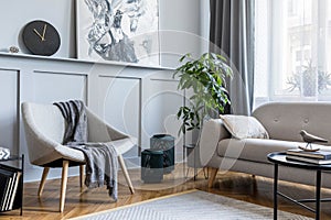 Stylish scandinavian home interior of living room with design gray sofa, armchair and personal accessories.