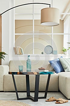 Stylish scandinavian living room interior with neutral modular sofa, design coffee table, window, floor lamp, plant, decoration.
