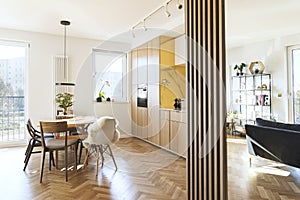 Stylish scandinavian open space interior of kitchen and dining room with design family table and chairs and other kitchen.