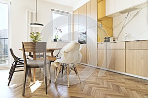 Stylish scandinavian open space interior of kitchen and dining room with design family table and chairs and other kitchen.