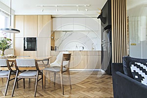 Stylish scandinavian open space interior of kitchen and dining room with design family table and chairs and other kitchen.