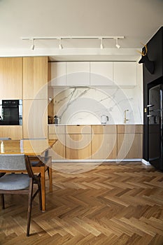 Stylish scandinavian open space interior of kitchen and dining room with design family table and chairs and other kitchen.