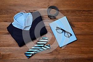 Stylish school uniform for boy, glasses and notebook on wooden background, flat lay
