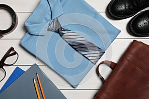 Stylish school uniform for boy, glasses and stationery on white wooden background, flat lay