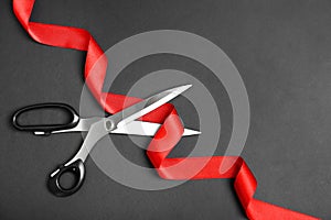 Stylish scissors and red ribbon on black background, flat lay. Ceremonial tape cutting