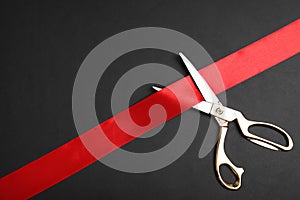 Stylish scissors and red ribbon on black background, space for text. Ceremonial tape cutting