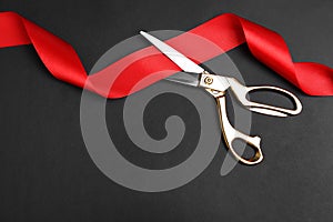 Stylish scissors and red ribbon on black, flat lay with space for text. Ceremonial tape cutting