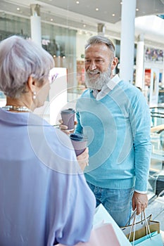 Stylish senior couple drinking coffee taking break during shopping in mall