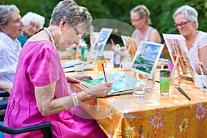 Stylish senior lady painting in art class with friends from her care home for the aged copying a painting with water colors.