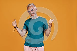 Stylish senior man gesturing and smiling while standing against orange background