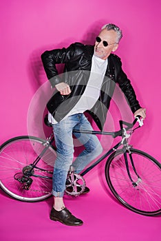 Stylish senior man wearing leather jacket, sunglesses and riding bicycle