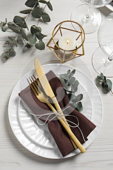 Stylish setting with cutlery and eucalyptus leaves on white wooden table, flat lay