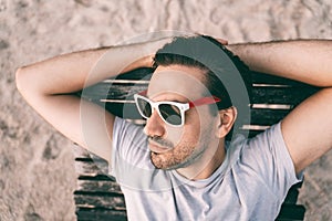 Stylish sexy young brunette man with a beard, a Latin lover, in sunglasses, lies on a sunbed. Top shot