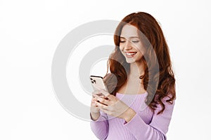 Stylish shopping girl with red hair place order, chatting on mobile phone and smiling, paying on smartphone, chatting