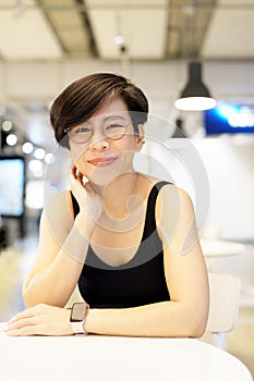 Stylish, short hairstyle Asian woman with eyeglasses smiling, looking at camera in modern cafe