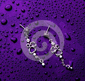 Stylish silver jewelry with water drops isolated on a violet background