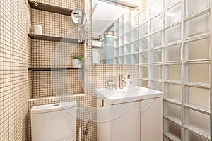 Stylish and simple bathroom design with beige mosaic and toilet and glass block wall with shelves. Concept hotel