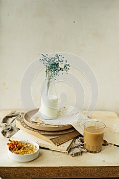 Stylish simple monochrome beige table setting at home. gypsophila in glass bottle of milk on stack of old books, cup of coffee,