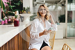 Stylish slim woman iin cafe while texting on smartphone and drinking cooling juice