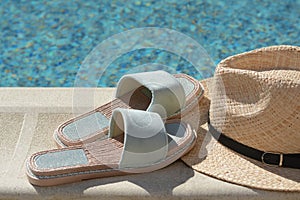 Stylish slippers and straw hat at poolside on sunny day. Beach accessories