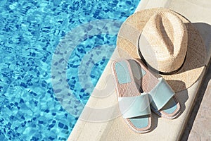 Stylish slippers and straw hat at poolside on sunny day, space for text. Beach accessories