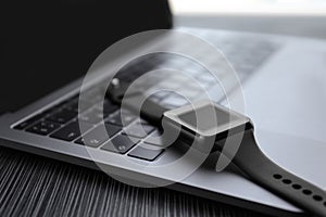 Stylish smart watch and laptop on table, closeup