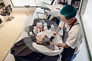 Stylish smiling female barber washes the hair of woman in beauty salon