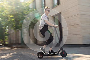 Stylish Smiling Man Riding Modern Kick Scooter Near Modern Building. Contemporary Eco Transport