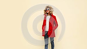 Stylish smiling young woman wearing red coat jacket with fur hood walking looking away on background, blank copy space for