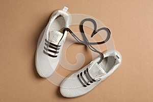 Stylish sneakers and shoe laces in shape of heart on brown background, flat lay