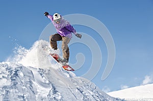 Stylish snowboarder with helmet and mask jumps from high snow slope