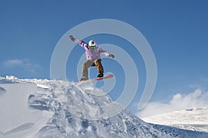 Stylish snowboarder with helmet and mask jumps from high snow slope