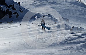 Štýlový snowboardista kráča so svojím krásnym snowboardom cez veternú smršť. Silná víchrica zúriaca na vrchole hory a muž v